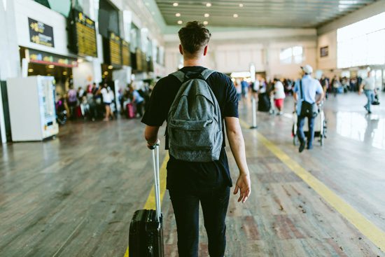 Going to Rehab Away from Home: What You Need to Know - young man with luggage at airport facing away