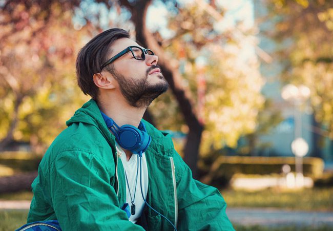 brunette bearded man with glasses in green coat taking deep breath outdoors - mental health
