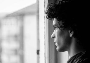 black and white - young man looking out window - Seasonal Affective Disorder 