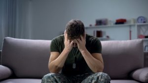 military man sitting on couch with head in hands - veteran