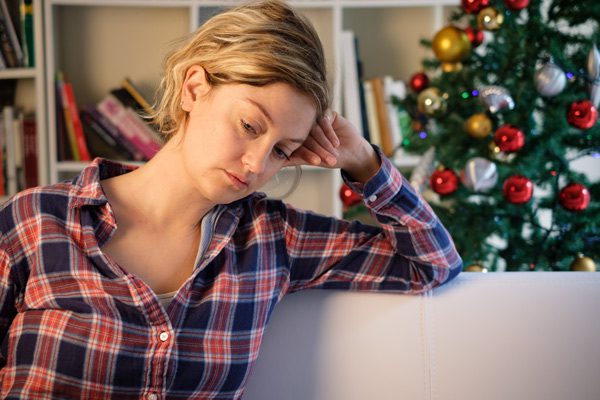 sad looking woman sitting on couch with Christmas tree in background - interventionist