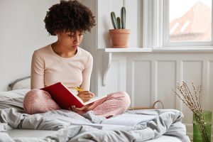 lovely African American woman writing in journal - self-care during covid