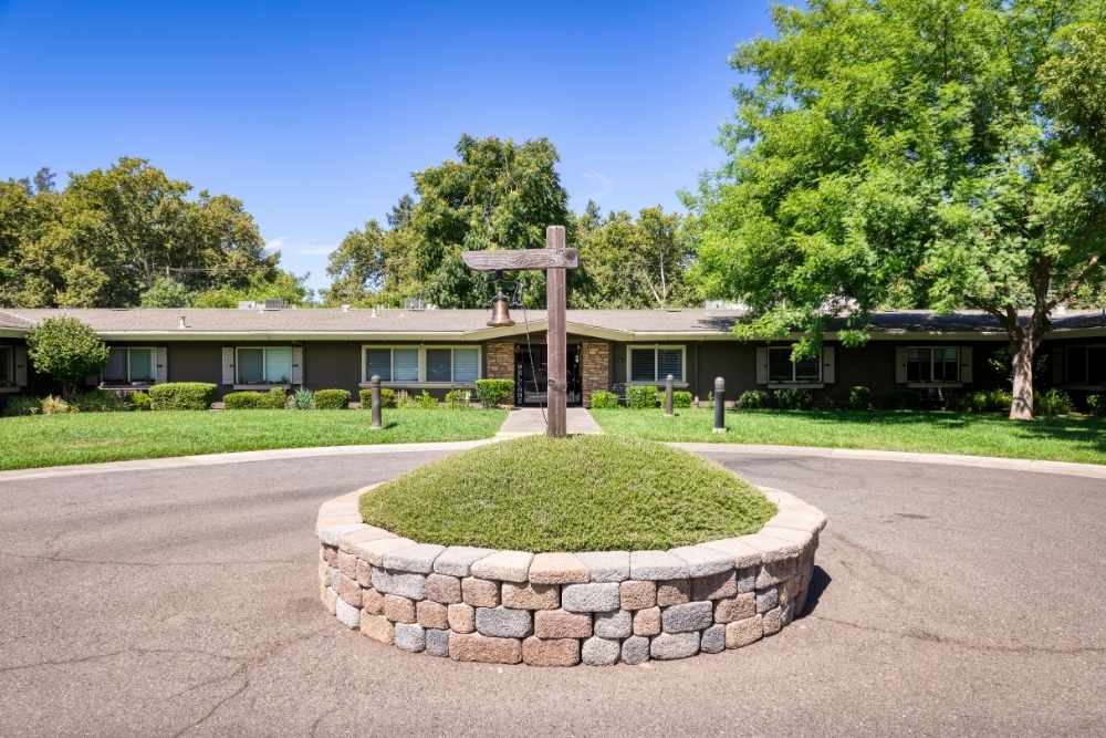 Exterior view of a single-story building with a landscaped circular driveway, green lawn, and trees under a clear blue sky.