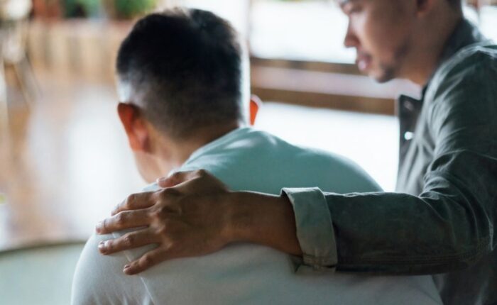 A person places a comforting hand on another’s shoulder, offering support and empathy during an emotional moment.