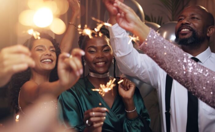 A group of adults smiling and celebrating together while holding sparklers at a festive indoor gathering.